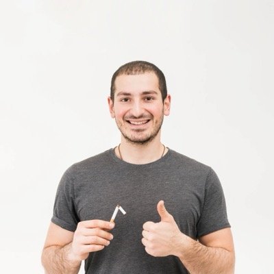 Smiling man holding broken cigarette showing thumb up sign against white background scaled